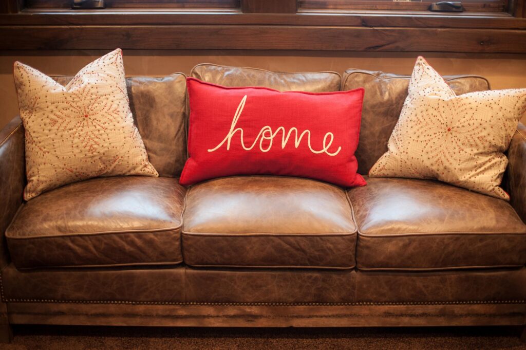 a brown leather couch with a red pillow that says home.