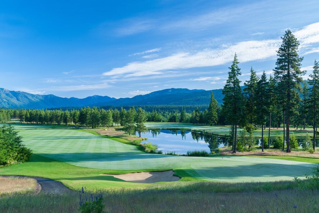 a golf course with a lake and mountains in the background.